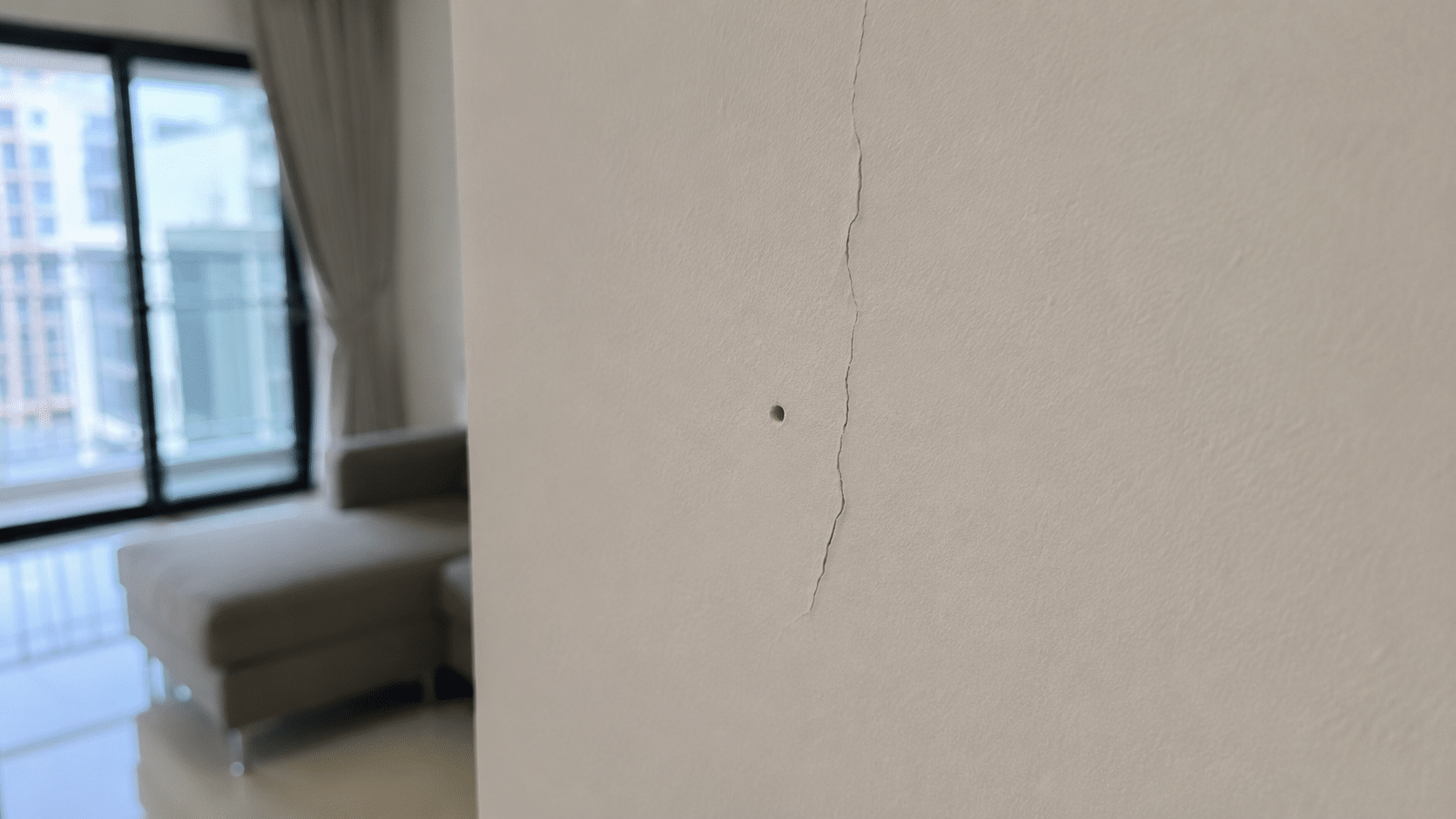 Small wall crack and nail hole on an indoor painted wall.
