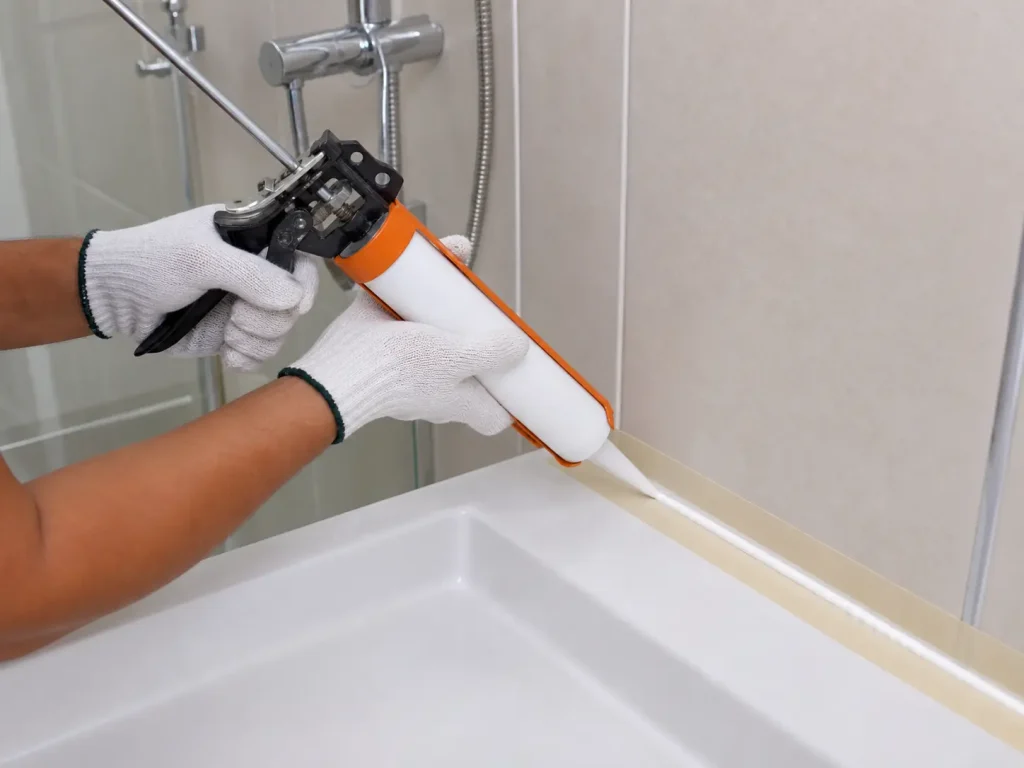 Malaysian homeowner applying a smooth white sanitary silicone bead along a shower joint