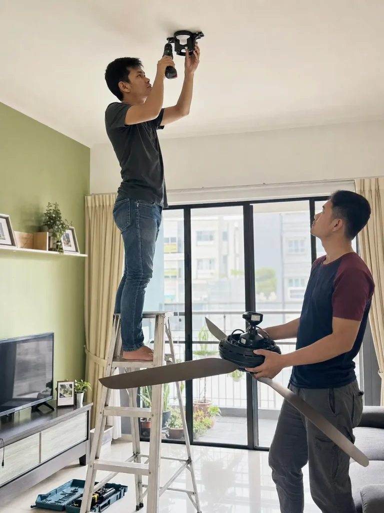 Malaysian homeowner installing a ceiling fan bracket from a stable ladder at home