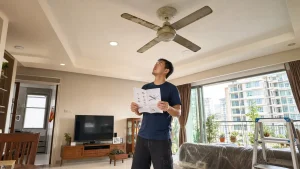 Malaysian homeowner checking an old ceiling fan in a condo living room before replacement